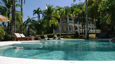 a swimming pool in front of a house with palm trees at Villa Quebrada Estate in Montezuma