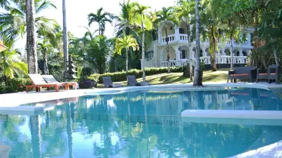 a swimming pool in front of a house with palm trees at Villa Quebrada Estate in Montezuma