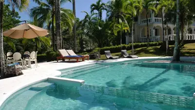 a swimming pool with chairs and an umbrella and a house at Villa Quebrada Estate in Montezuma