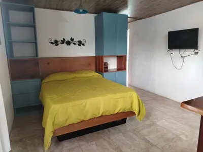 a bedroom with a bed with a yellow comforter and a tv at Apartamento Roble Sabana in Tapantí