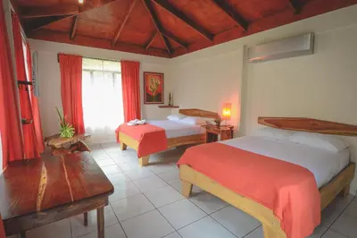 a bedroom with two beds and a table and a window at Hotel Cerro Lodge in Tarcoles