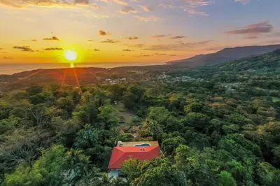 a house in the forest with the sunset in the background at Eco-Luxurious Villa 4bdr - 5 min to the Beach in Uvita