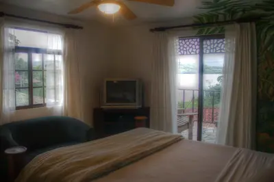 a bedroom with a bed and a tv and windows at Gingerbread Restaurant & Hotel in Nuevo Arenal