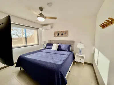 a bedroom with a blue bed and a window at Modern Beach Apartment - Walk to Playa Mantas & Beach Club Access in Punta Leona