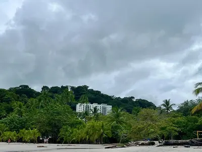 a white building on a beach with palm trees at Modern Beach Apartment - Walk to Playa Mantas & Beach Club Access in Punta Leona