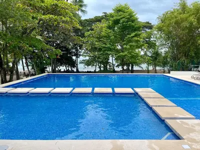 a swimming pool with blue water and trees at Modern Beach Apartment - Walk to Playa Mantas & Beach Club Access in Punta Leona
