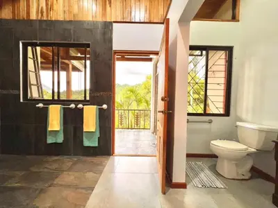 a bathroom with a toilet and a window and a door at Romantic Retreat Volcano View! River Trail! in El Castillo de la Fortuna