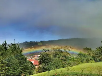 a rainbow over a town in a field with trees at Monteluna Fraijanes in Poasito