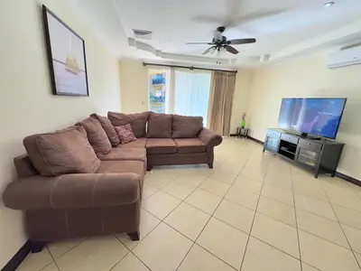 a living room with a brown couch and a flat screen tv at Paradise Beach Apartment Herradura in Herradura