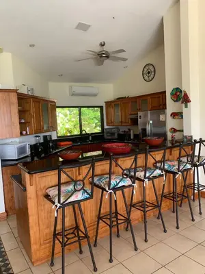 a kitchen with wooden cabinets and bar stools at Roma del mar - Vila s bazénem a krásným výhledem na moře in Paquera