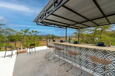 a patio with a bar and chairs on a deck at Nelblu Flamingo Suites in Playa Flamingo