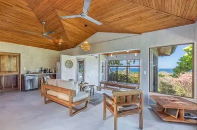 a living room with wooden ceilings and a table and benches at Driftwood ocean view in Playa Ostional