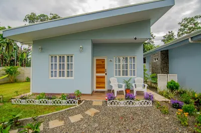 a white house with two chairs and flowers at Villas Mali La Fortuna in Guayabal