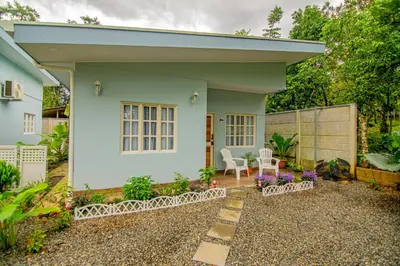 a small white house with a chair in the yard at Villas Mali La Fortuna in Guayabal