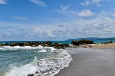 a beach with rocks and the ocean on a sunny day at Palacio Tropical in Puntarenas