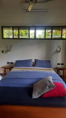 a bedroom with a bed with blue sheets and windows at Casa Caladium in Manuel Antonio