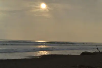 a beach with the sun setting over the ocean at Hostel Piramys in Tapantí