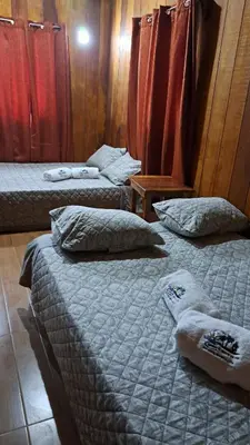 three beds in a room with red curtains at Cabaña Nayuribe in Santa Cruz