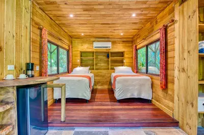 two beds in a room with wooden walls and windows at Ylang Ylang Beach Resort in Montezuma