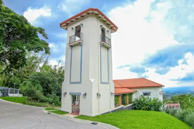 a small white building with a balcony on a green lawn at Hotel El Arca, Jardín Botánico y Restaurante in Santa Bárbaraa