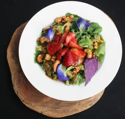 a bowl of salad with strawberries and lettuce on a plate at Hotel El Arca, Jardín Botánico y Restaurante in Santa Bárbaraa