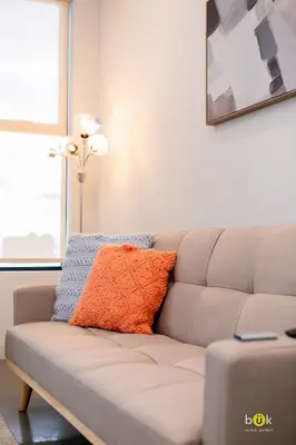 a couch with an orange pillow on it in a living room at INSTAWORTHY CORNER VIEW 200Mbps in San José