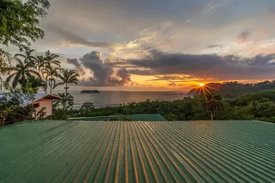 a view of the sunset from a house with a green roof at Hotel Villas de la Selva in Manuel Antonio