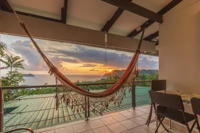 a hammock in a room with a view of the ocean at Hotel Villas de la Selva in Manuel Antonio