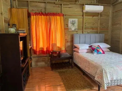 a bedroom with a bed with an orange curtain at Cabaña Jacaranda #2, junto al río, San Isidro, Pérez Zeledón in Roble
