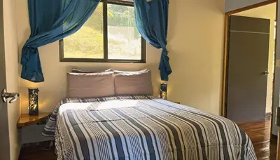 a bedroom with a bed with blue curtains and a window at Mei Tai Cacao Lodge in Bijagua
