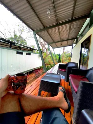 a man sitting on a deck with a cup of coffee at Casa Abierta Playa Juquillal 2 habitaciones in Santa Cruz