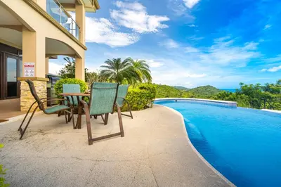 a patio with a table and chairs next to a swimming pool at 1hr SJO Airport-Ocean views-Gated Beachclub-Pool in Tarcoles
