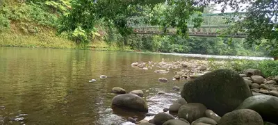 a river with rocks and a bridge in the background at La casita de Antonio en Sarapiqui in Llano Grande