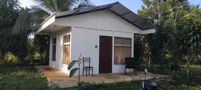 a small white house with two chairs in the yard at La casita de Antonio en Sarapiqui in Llano Grande