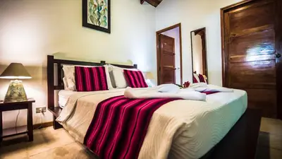 a bedroom with a large bed with red and white sheets at Hotel El Pequeño Gecko Verde in Sámara
