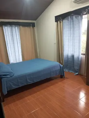 a bedroom with a bed with blue sheets and windows at Linda vista in Bijagua