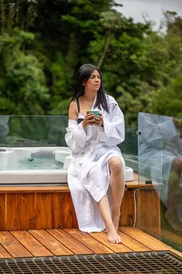 a woman sitting on a wooden table in front of a tub at Aves Monteverde Eco Lodge con jacuzzi in La Cruz