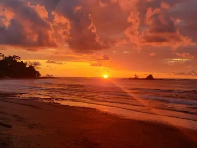 a sunset on a beach with the ocean at Cabinas La Parcela in Dominicalito