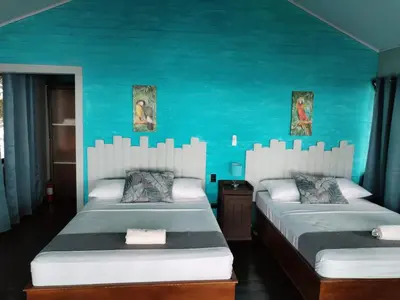 two beds in a room with a blue wall at Cabinas La Parcela in Dominicalito