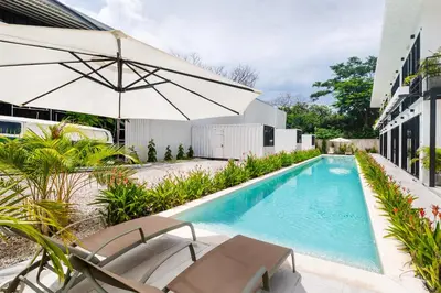 a swimming pool with chairs and an umbrella next to a building at Nomad Containers - Adults only in Tamarindo