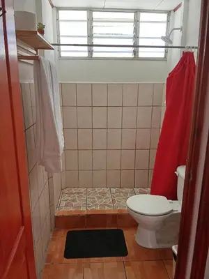 a bathroom with a toilet and a red shower curtain at Apartamentos y Cabinas Geckos in Sardinal