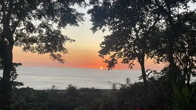a sunset over the ocean seen through trees at villa colibri in Nicoya
