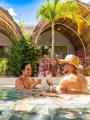 a man and woman sitting in a swimming pool with wine glasses at Les Voiles Blanches in Tamarindo