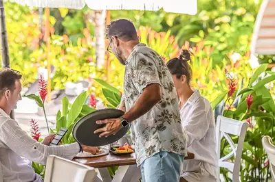 a man standing at a table holding a pan at Les Voiles Blanches in Tamarindo