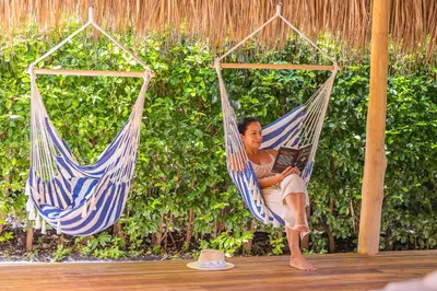 a man sitting in a hammock reading a book at Les Voiles Blanches in Tamarindo
