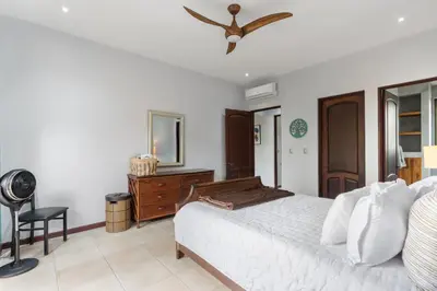 a bedroom with a bed and a dresser and a fan at Modern Island-Themed Condo with Floor-to-Ceiling Windows & Garden and Pool Views Within Walking Distance of the Beach in Coco