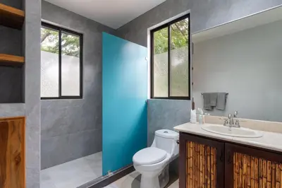 a bathroom with a toilet and a sink and two windows at Modern Island-Themed Condo with Floor-to-Ceiling Windows & Garden and Pool Views Within Walking Distance of the Beach in Coco