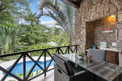 a patio with a table and chairs and a pool at Modern Island-Themed Condo with Floor-to-Ceiling Windows & Garden and Pool Views Within Walking Distance of the Beach in Coco