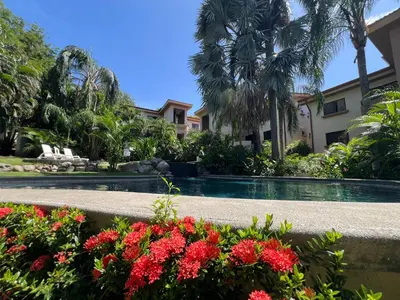 a swimming pool with flowers in front of a house at Serena Suites L2 Playas del Coco in Coco