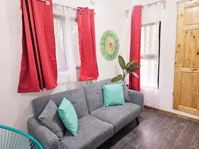 a living room with a gray couch and red curtains at Cara Coral, un oasis en la Selva in Tortuguero